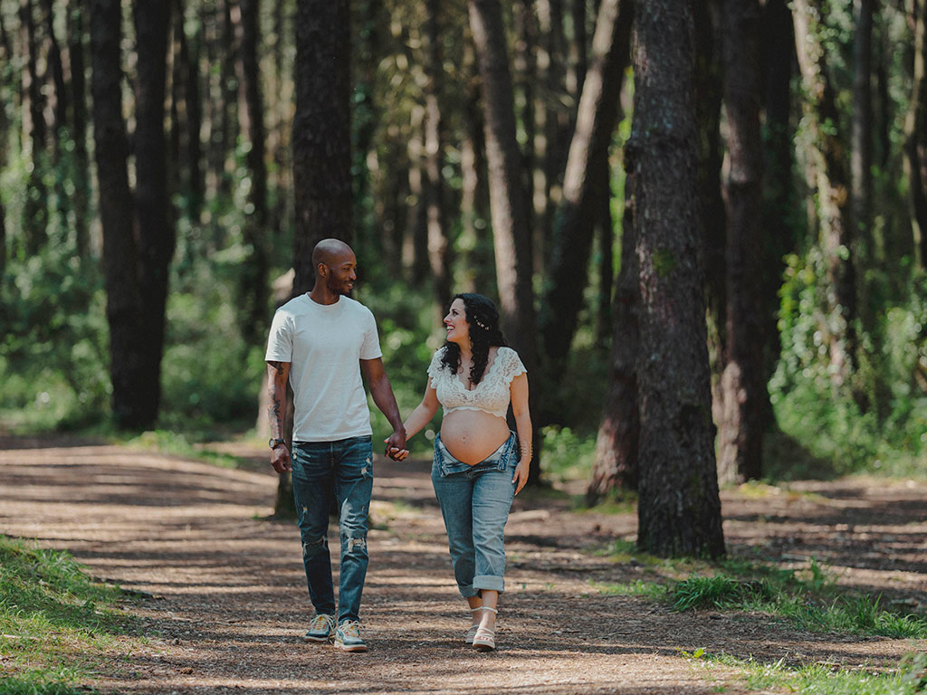 Pareja paseando entre pinares con su embarazo